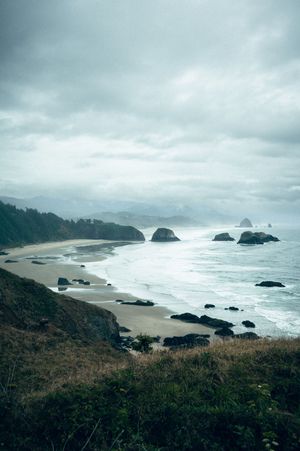 Aerial view of a moody Oregon coastline with sea stacks, sandy beach, and overcast skies at Cannon Beach.