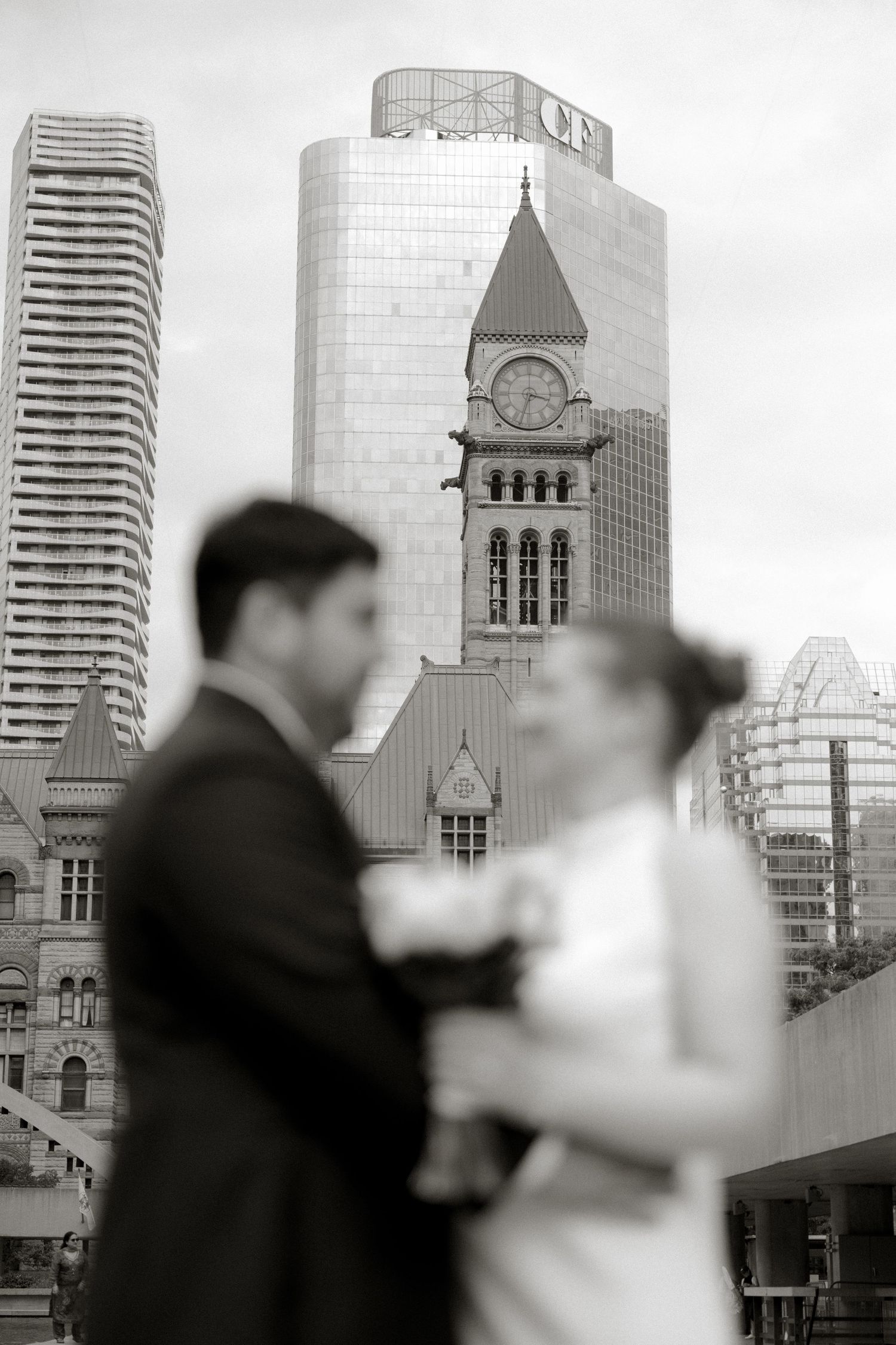 Bride and groom pose in soft focus with Toronto's historic Old City Hall clock tower rising behind them.