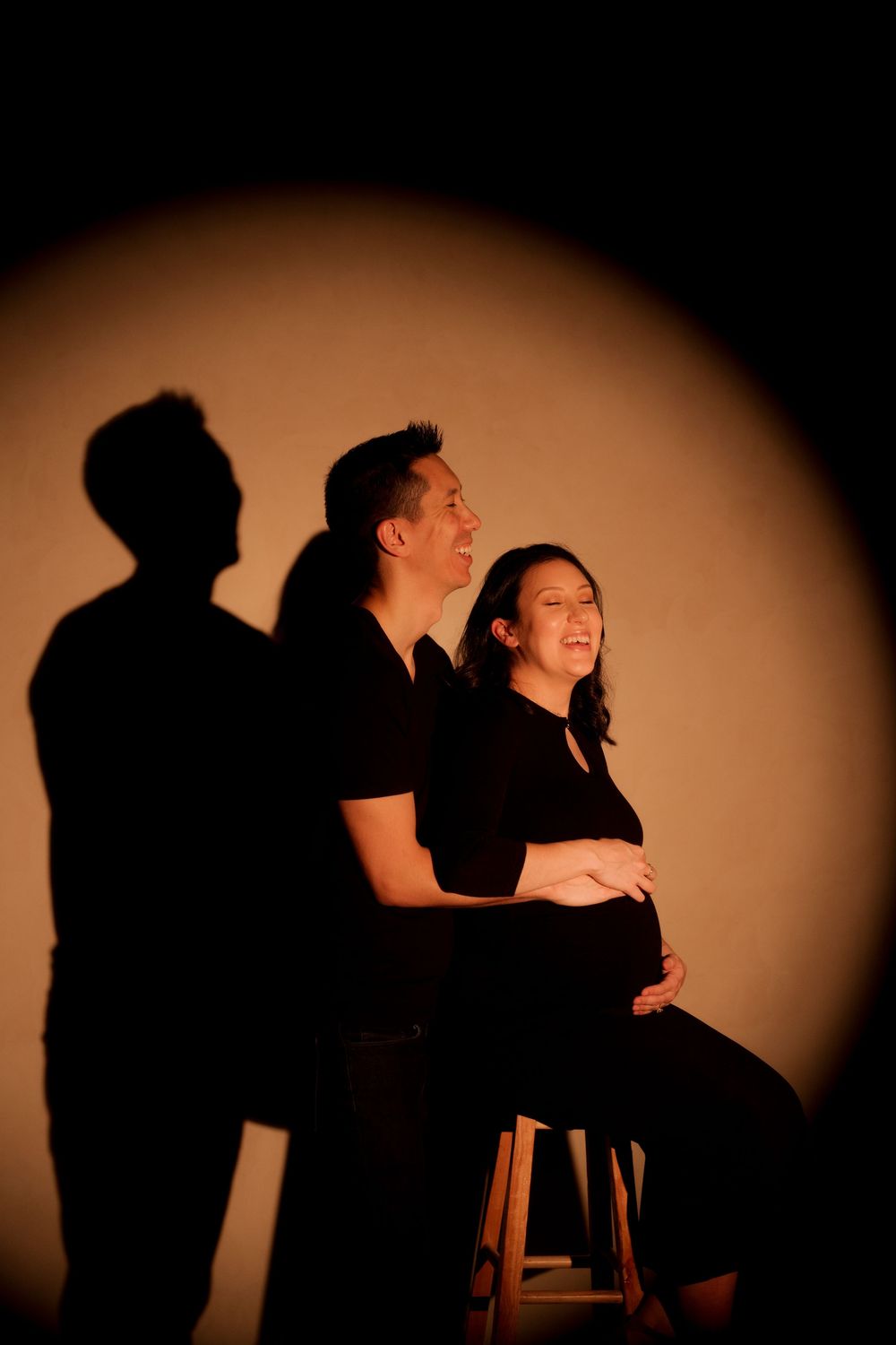Couple expecting a baby posing in spotlight, woman smiling while holding her pregnant belly.