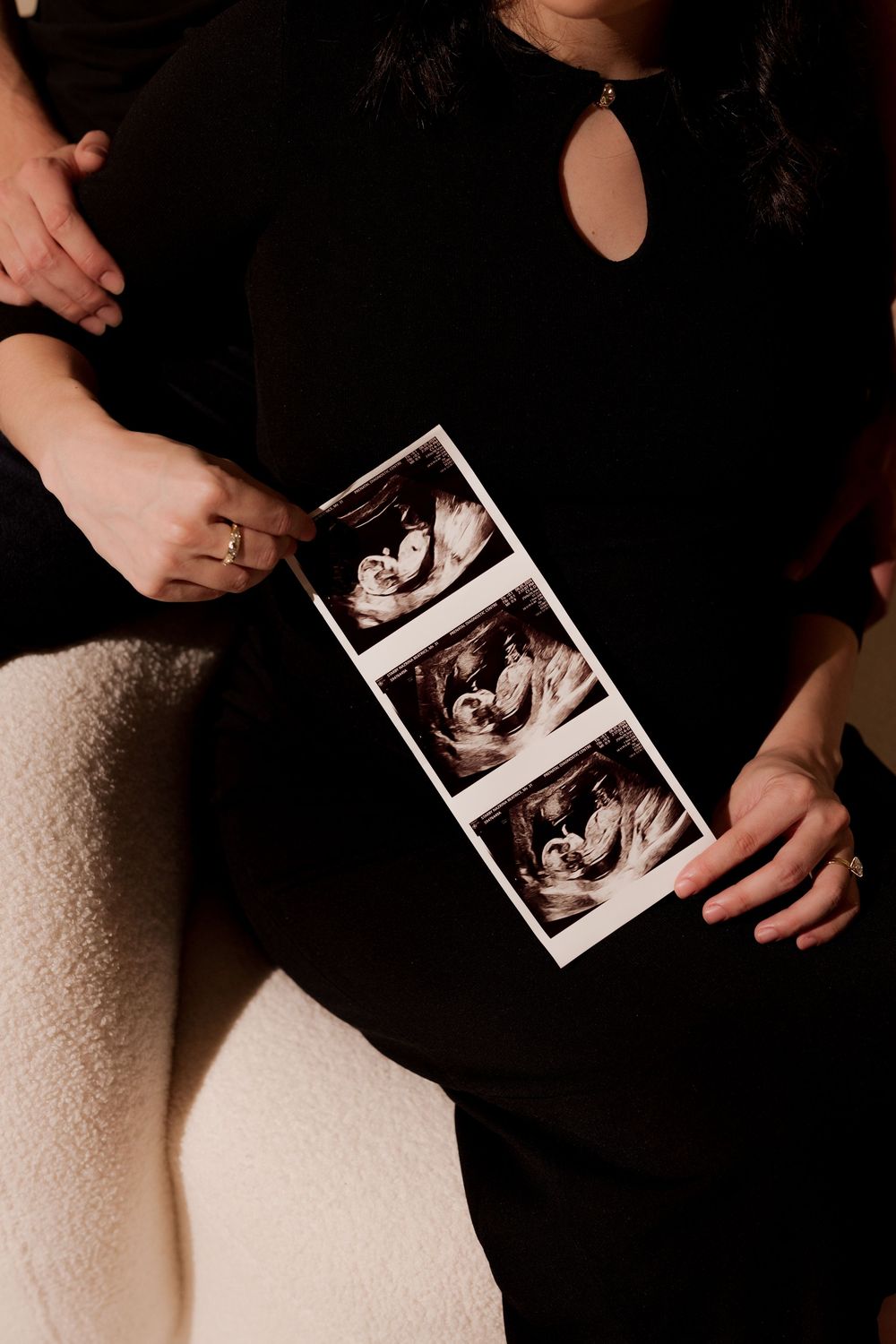 Pregnant woman in black dress holding ultrasound sonogram strip photos against her baby bump.