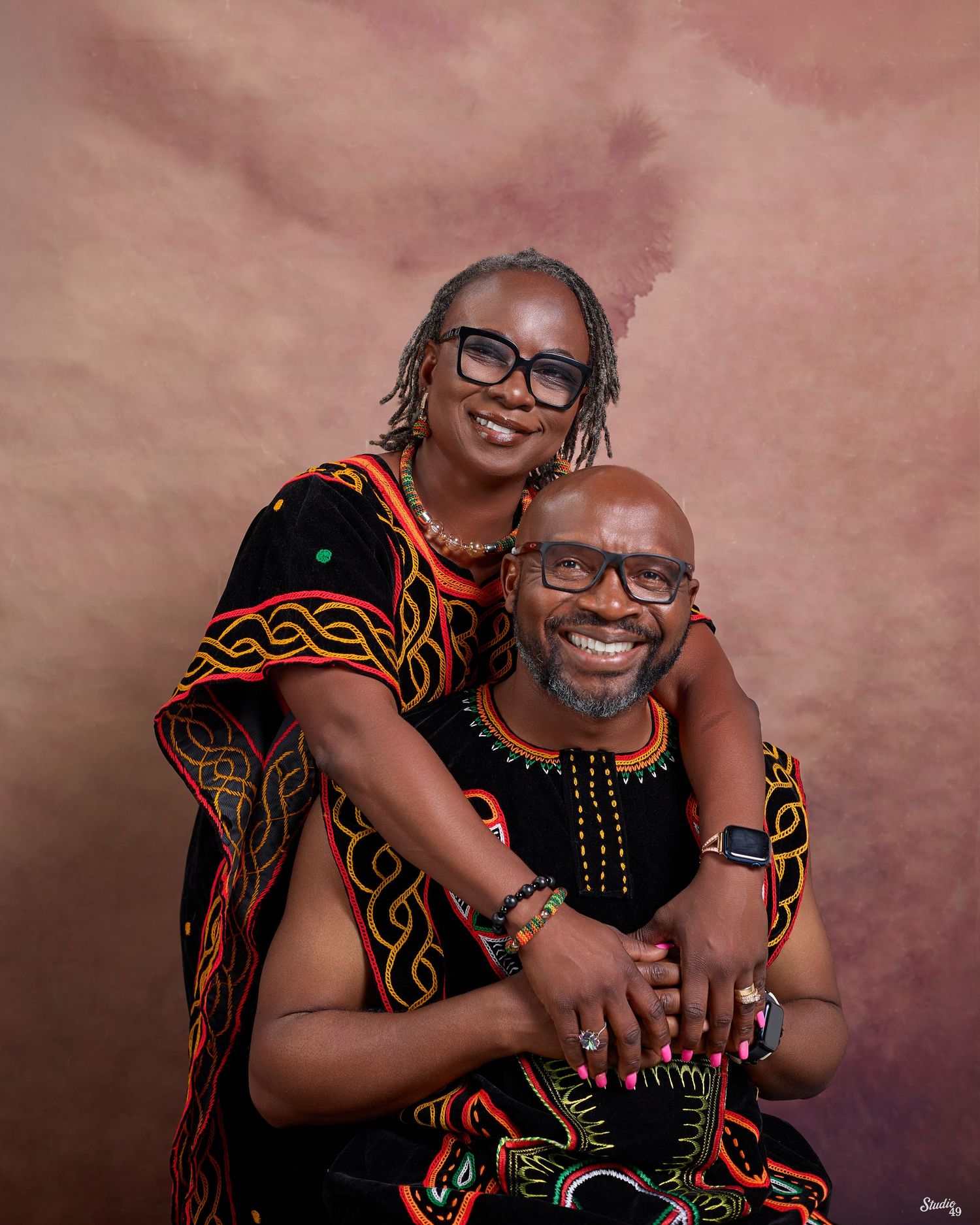 Couple in matching black African traditional attire with colorful embroidery posing together for a portrait.