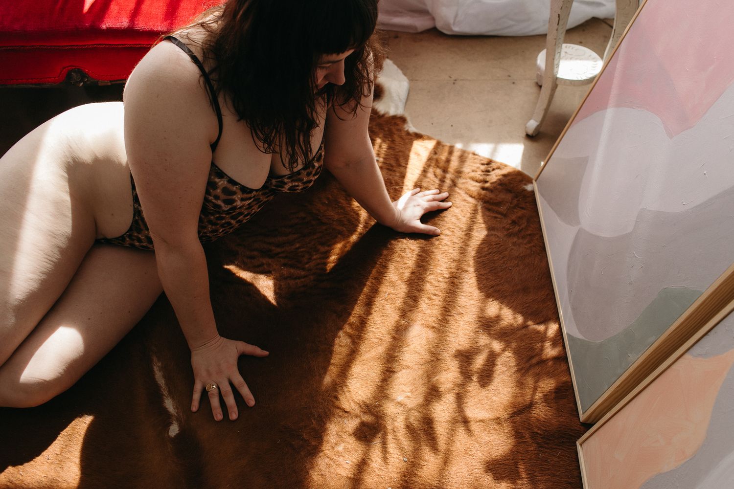 Woman in leopard print lingerie posing on a sunlit brown rug in a warmly lit bedroom.