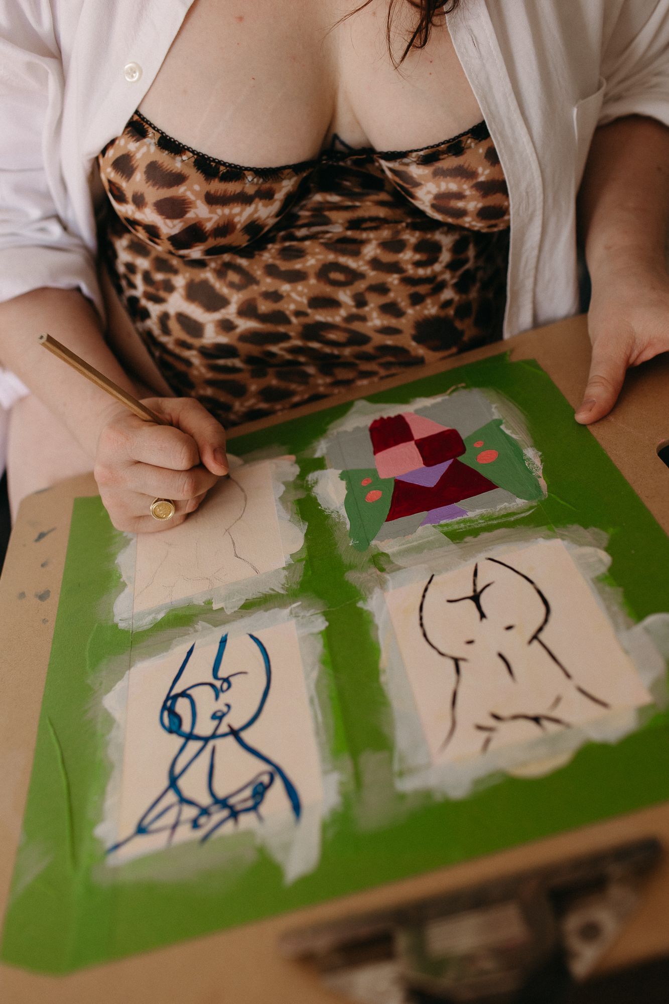 Artist painting abstract figure sketches on a green canvas board while wearing a leopard print top.