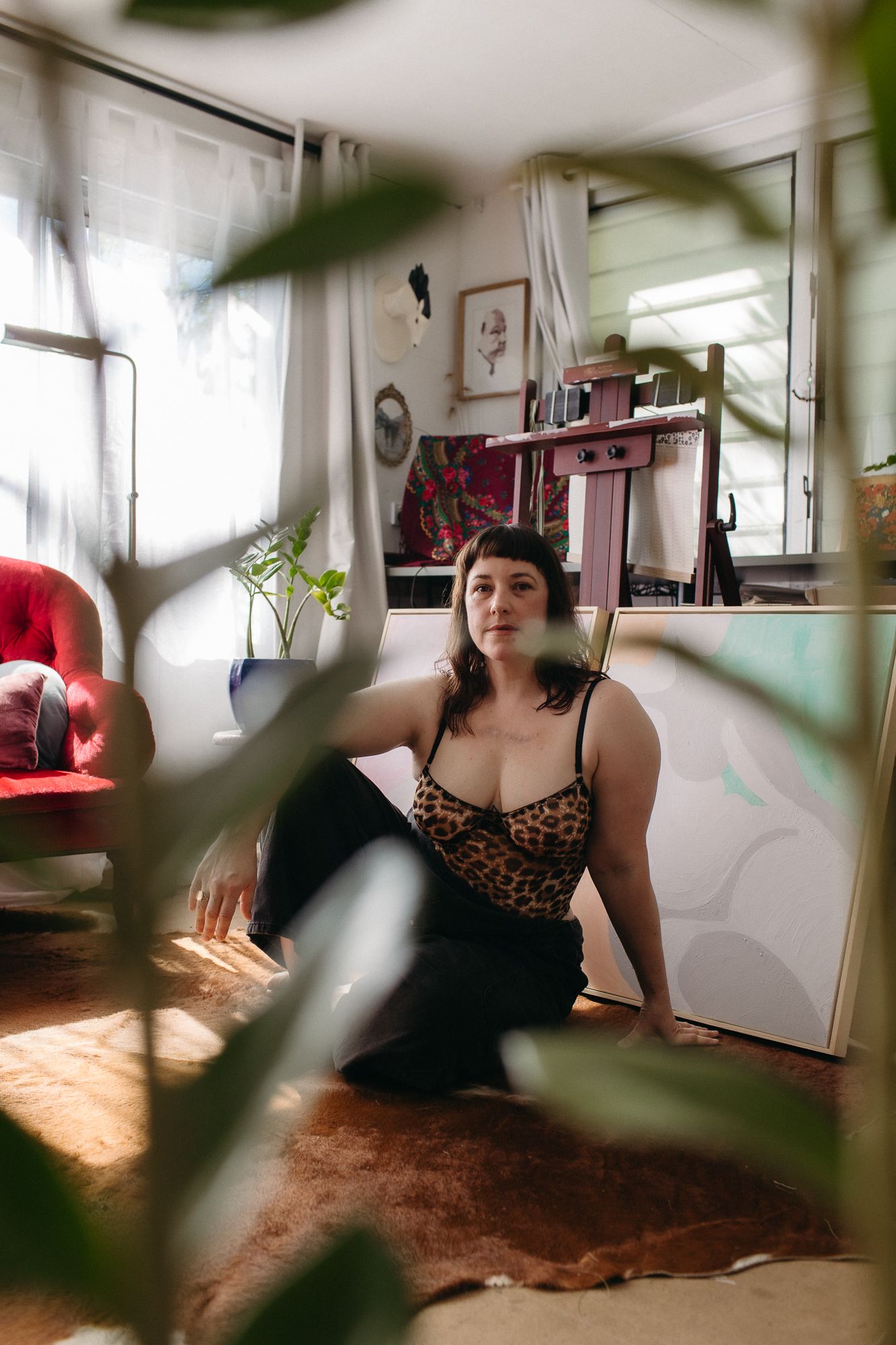 Woman in leopard print top sits on rug surrounded by plants in a cozy, art-filled bohemian living room.
