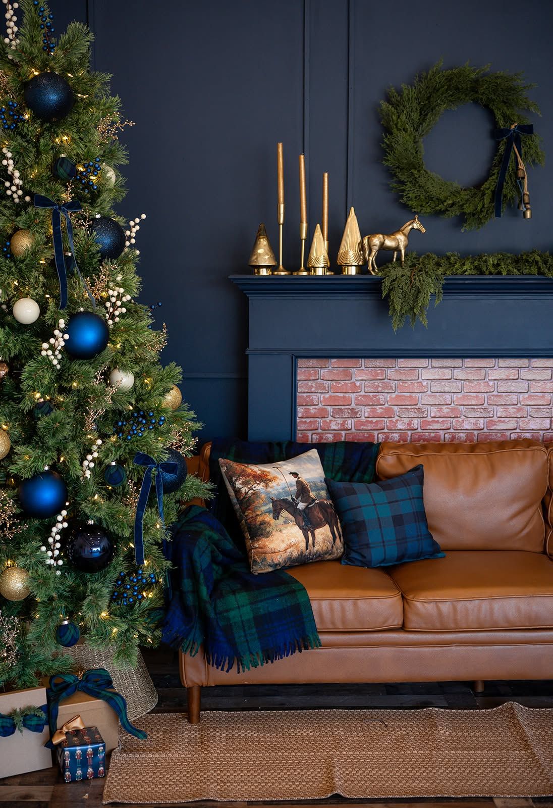 Cozy living room with a decorated Christmas tree, navy fireplace, gold candlesticks, tan leather sofa and plaid throw blanket.