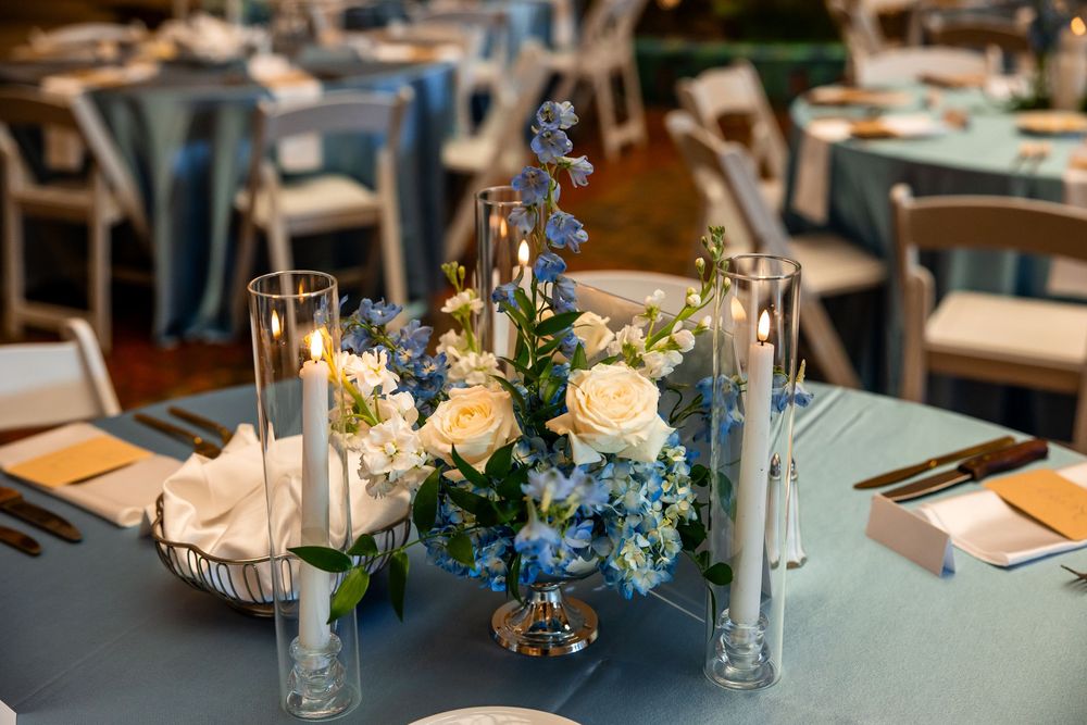 Blue and white floral centerpiece with candles on a blue tablecloth at an elegant wedding reception.