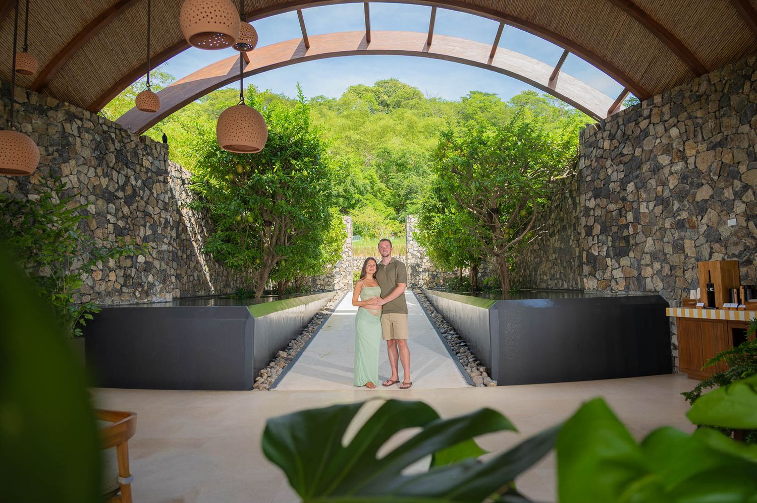 Couple embracing under stone archway surrounded by lush tropical greenery at a luxury resort garden pathway.