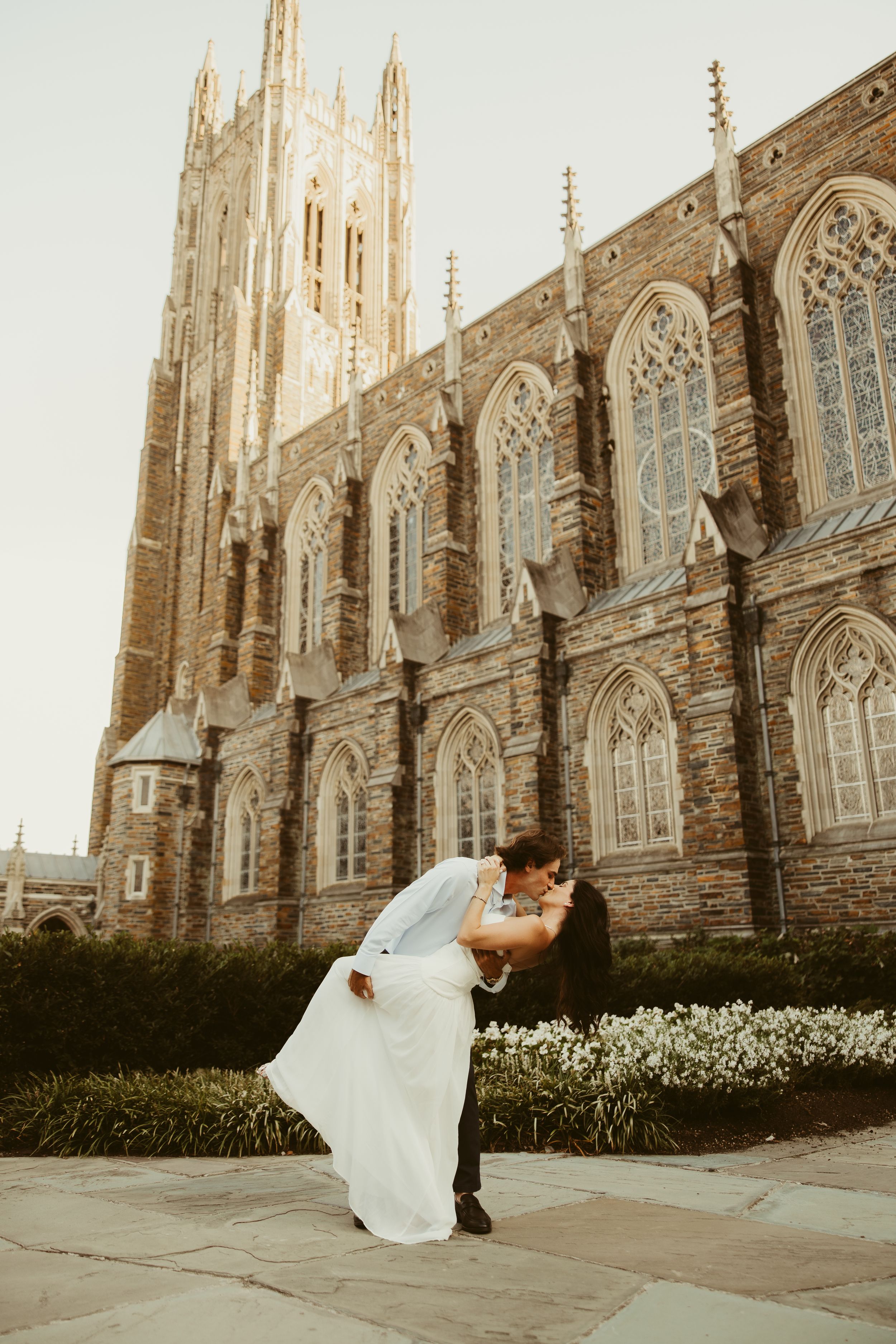 Couple sharing a romantic dip kiss in front of Duke Chapel's Gothic architecture on their wedding day.