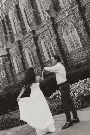 Black and white photo of a bride and groom dancing outside a Gothic stone church, her white gown flowing gracefully.