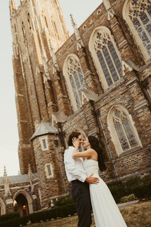 A bride and groom share a romantic moment in front of a stunning Gothic stone church during their wedding day.