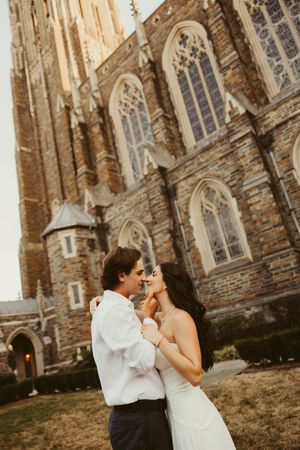 Bride and groom share a romantic kiss outside a grand Gothic stone church during their wedding day.