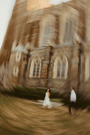 Bride and groom walk outside a historic stone church, captured with a dramatic spinning blur effect.
