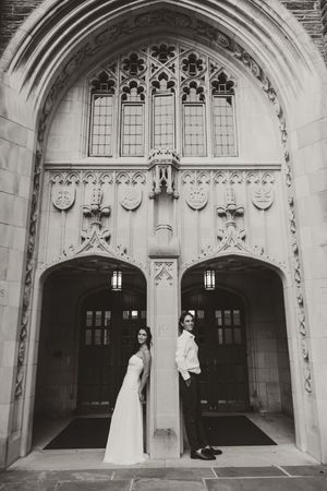 Black and white photo of bride and groom standing back-to-back under ornate Gothic stone archway.