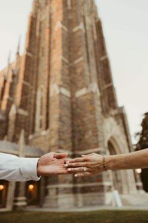 Two hands reaching toward each other in front of a grand Gothic cathedral, symbolizing love and connection.