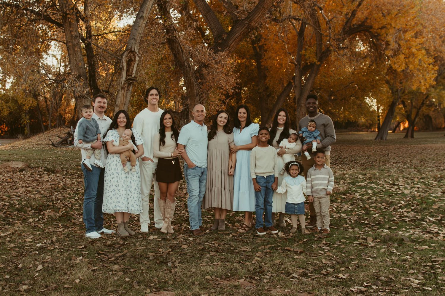 Large extended family group portrait in coordinated outfits during autumn season.
