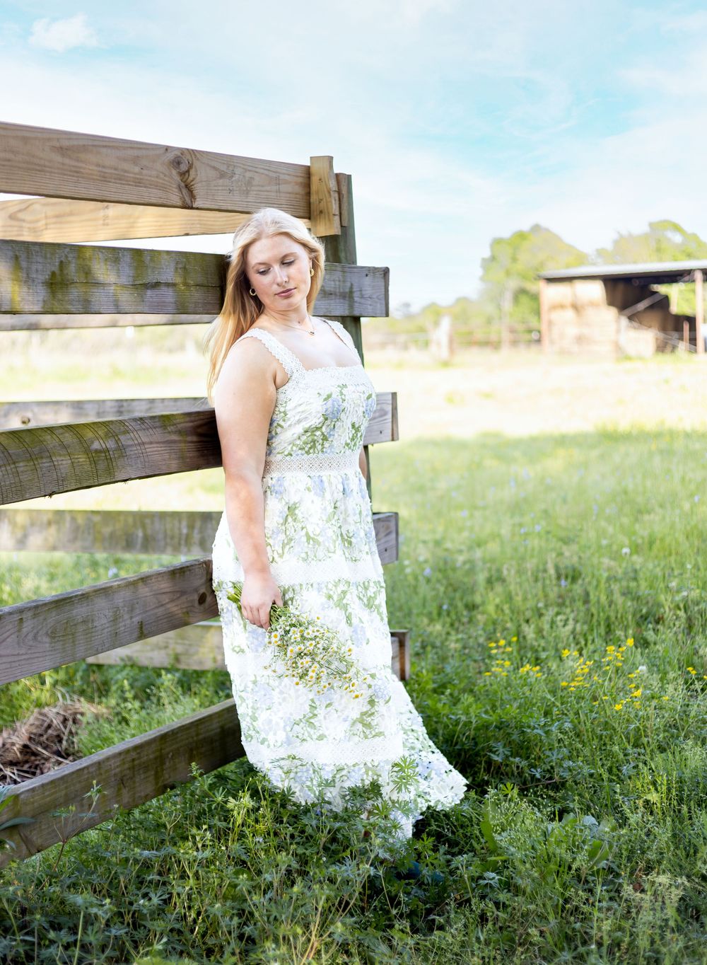 A white floral sundress stands out against a rustic wooden fence and green meadow in a sunny outdoor setting.