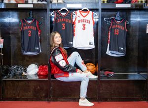 Young girl sits in a sports locker room with Wolves and Granger basketball jerseys displayed behind her.