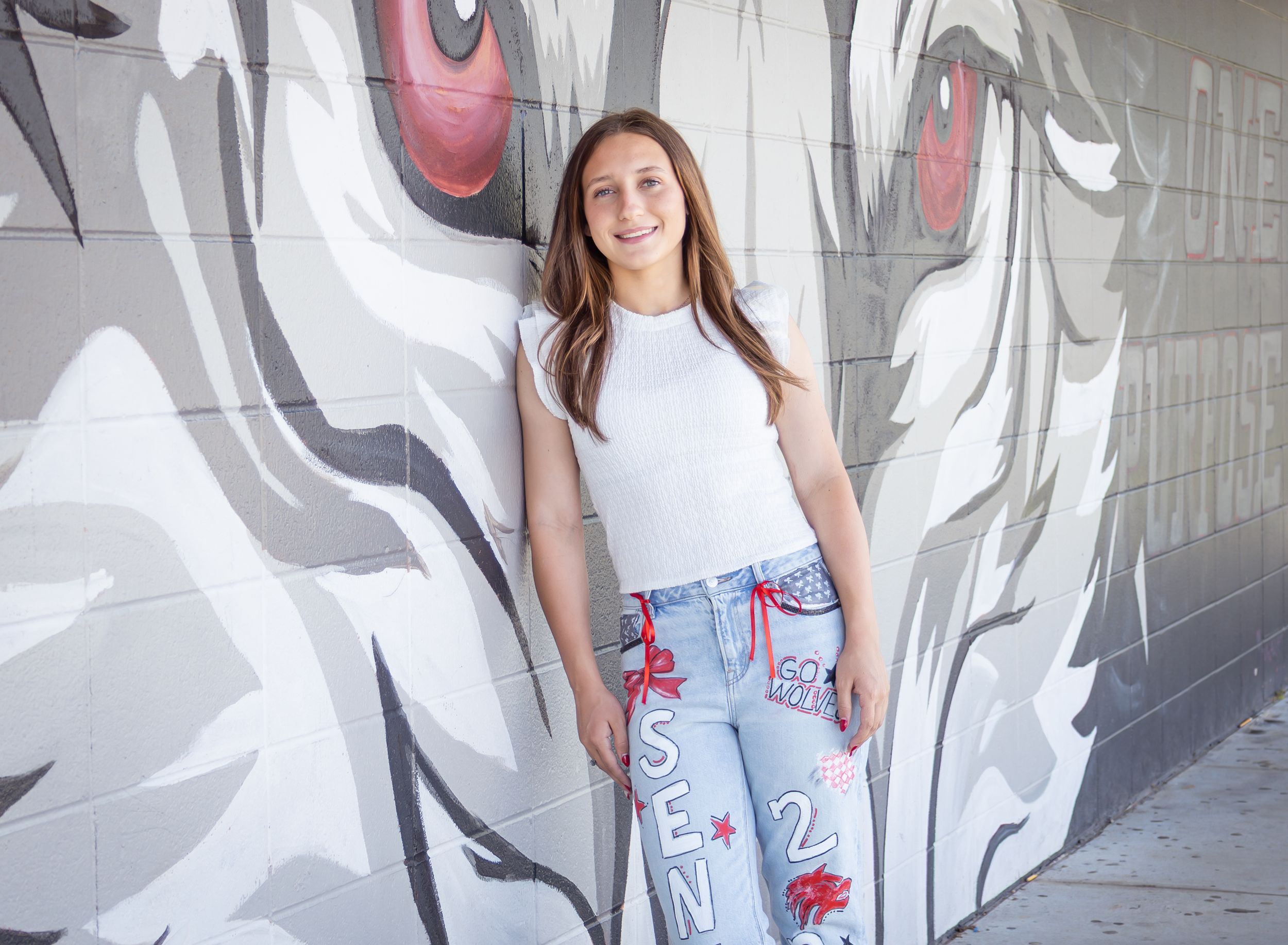 Teen girl in white top and custom jeans poses confidently in front of a large wolf mural on a gray wall.