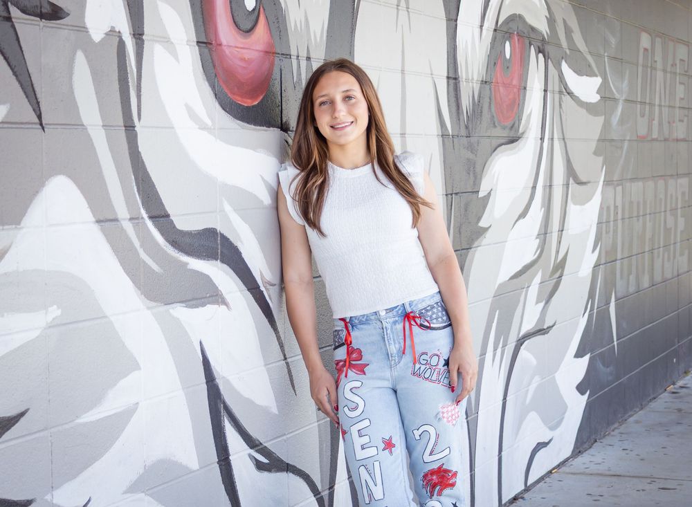 Teen girl in white top and custom jeans poses confidently in front of a large wolf mural on a gray wall.