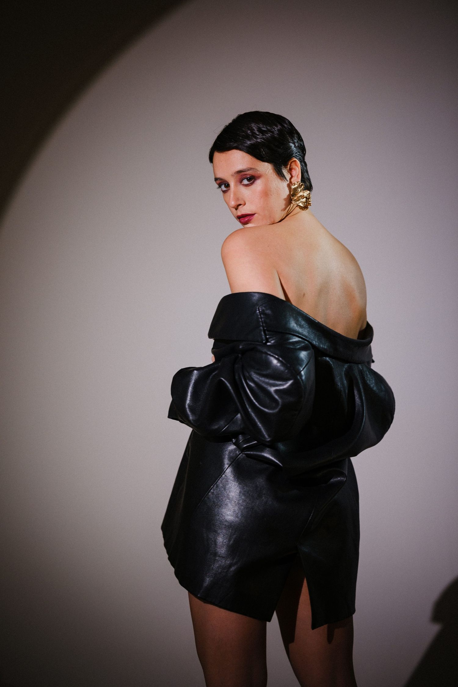 Artistic fashion photo of model in black leather jacket against moody backdrop.
