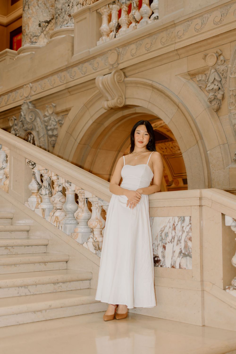 A graceful figure in a flowing white dress poses on an ornate marble staircase.