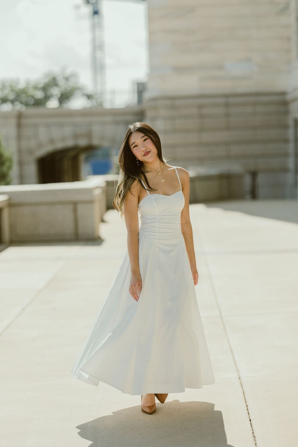 A gentle outdoor portrait capturing movement in a flowing white dress against stone architecture.
