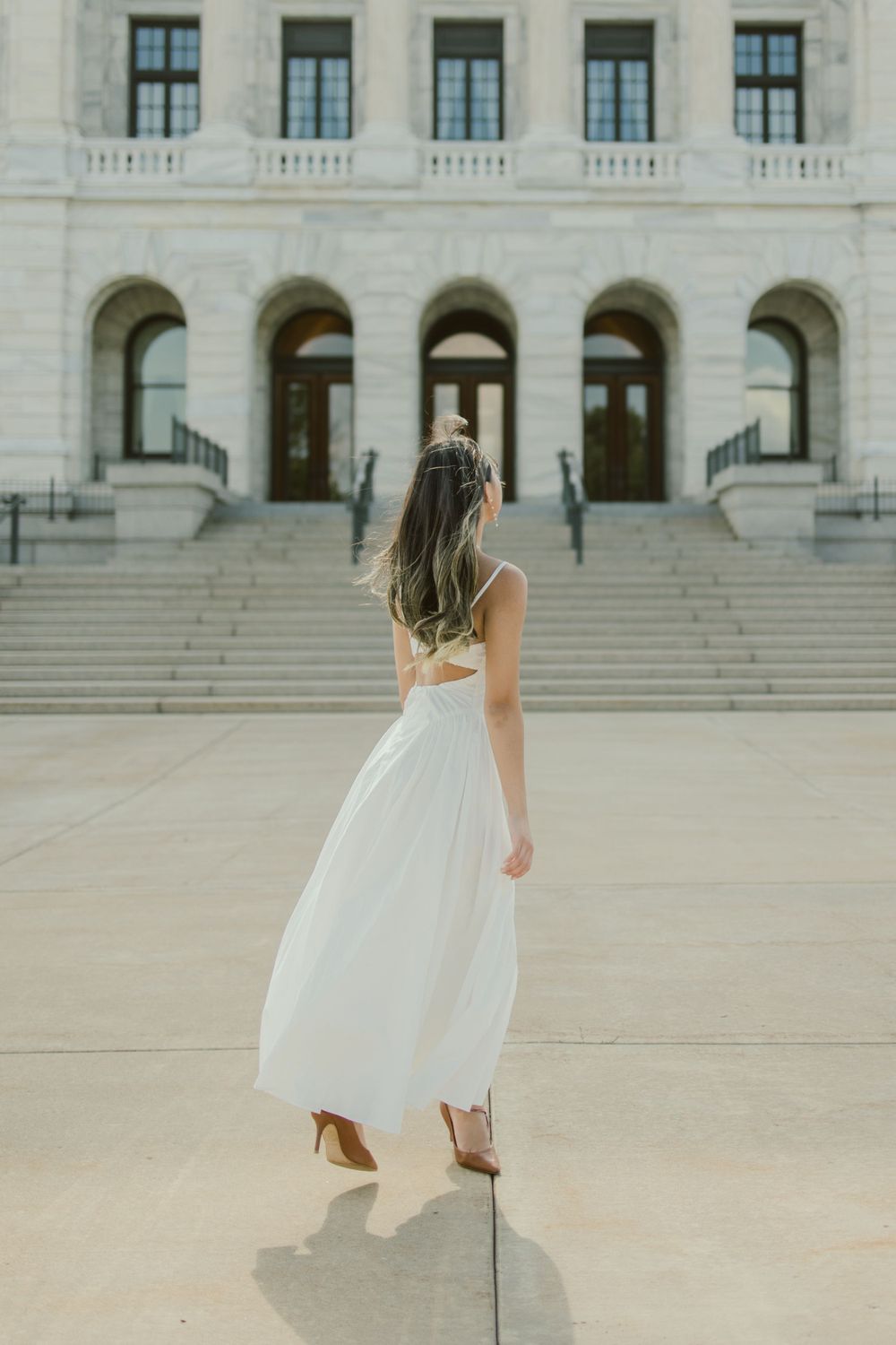 Back view of flowing white dress on stone steps of classical building.