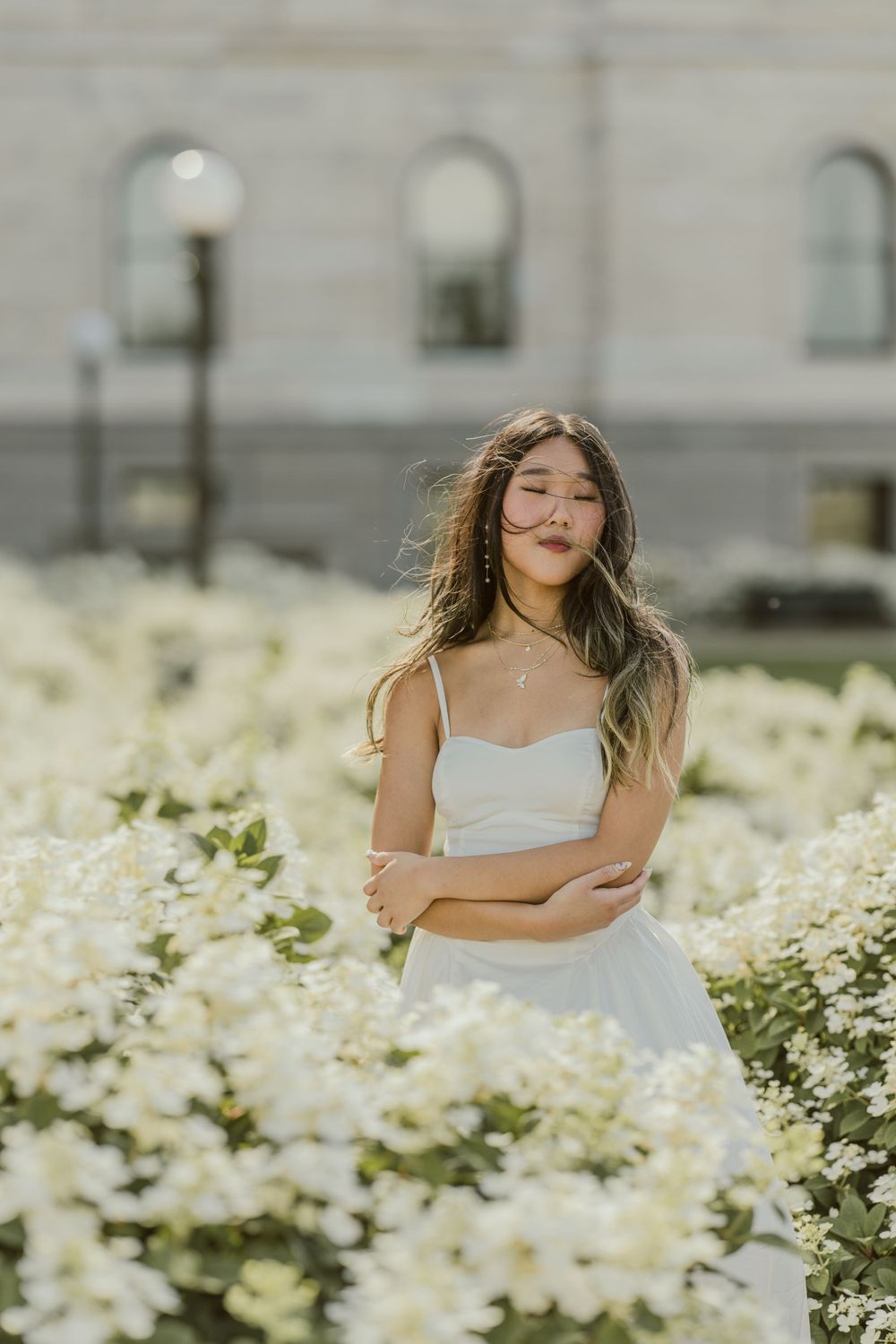 White dress amid blooming flowers with classical building in background.