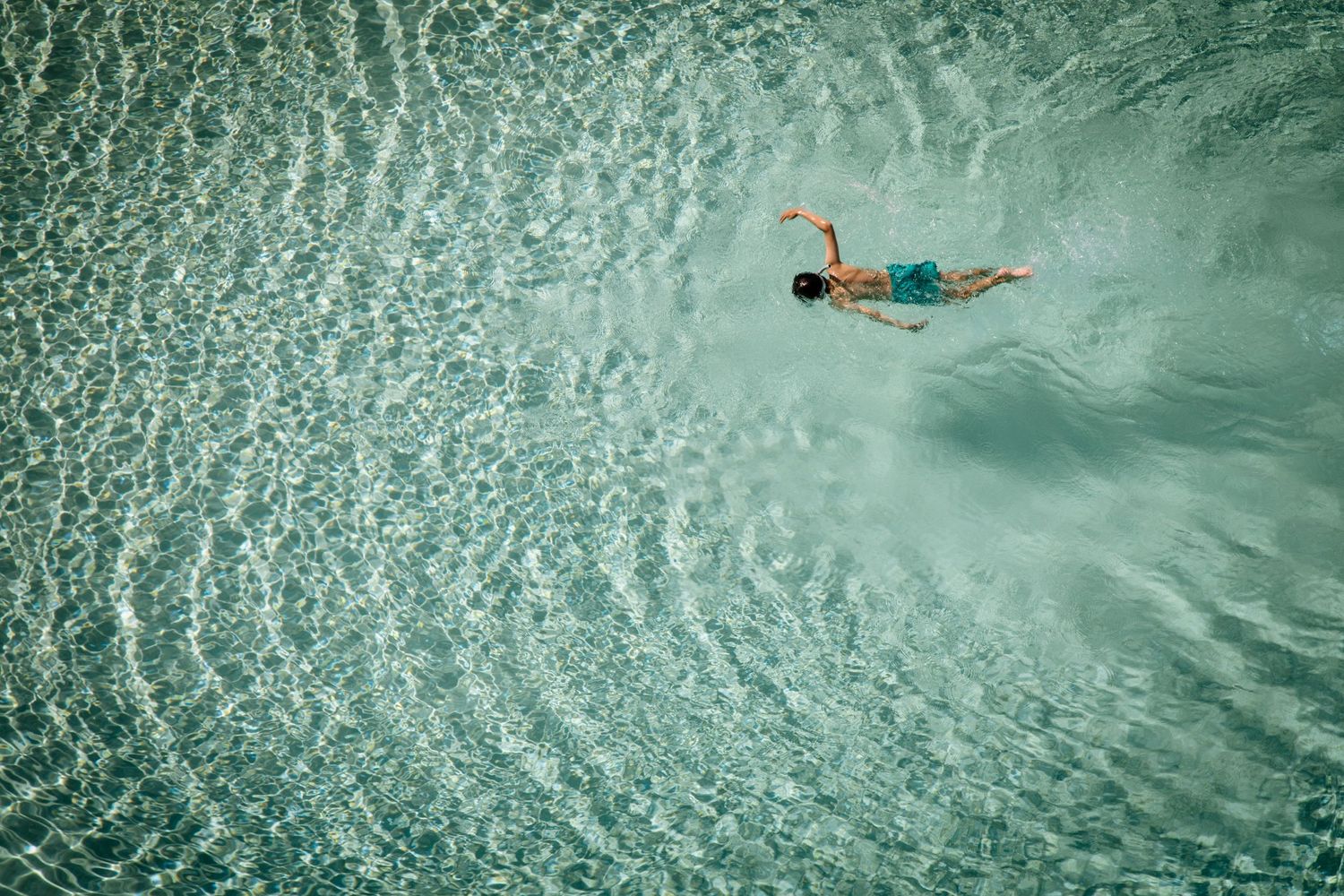 Aerial view of someone swimming in crystal clear rippling turquoise water.