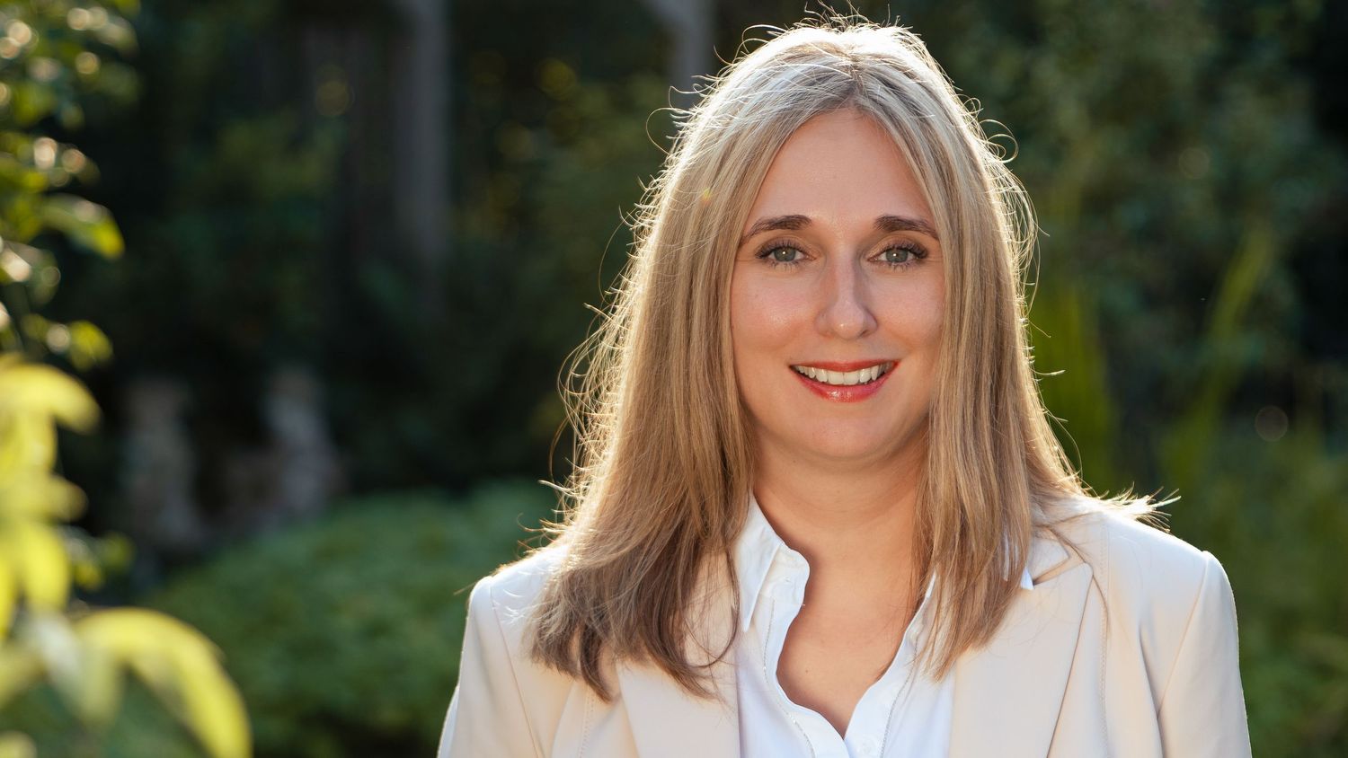 Business portrait of a smiling woman glowing in nature, showcasing professionalism and calm, with lush greenery in Zonhoven.
