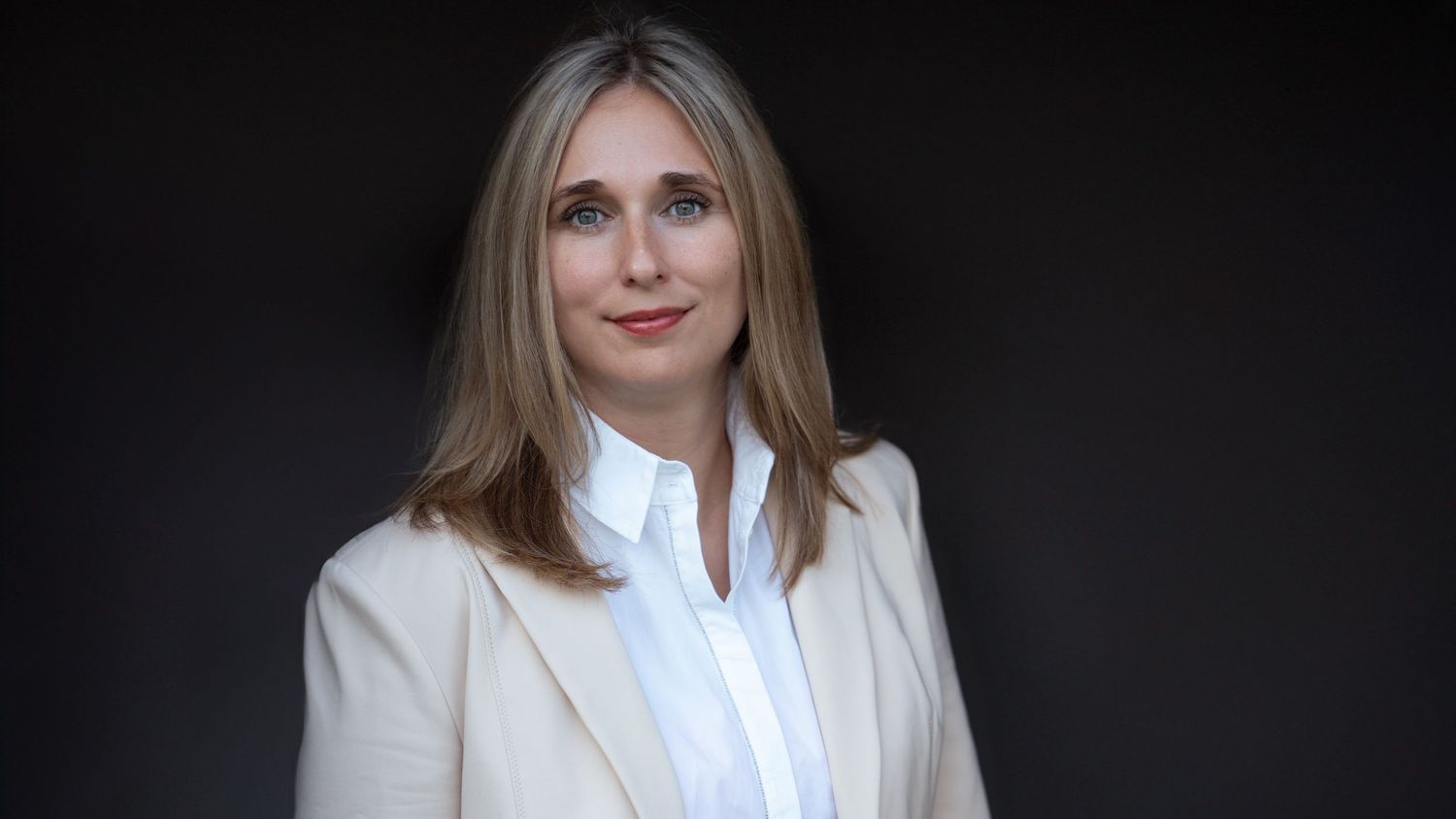 Professional portrait of a woman in a business suit, confidently posing against a dark background.