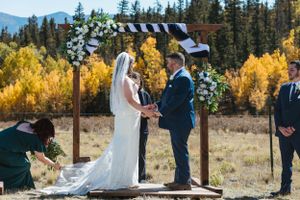 An outdoor mountain wedding ceremony under a wooden arch with golden aspen trees in the background.