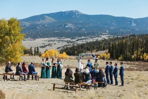 Outdoor mountain wedding ceremony with guests seated on benches against a backdrop of fall foliage and peaks.