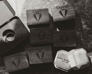 Wooden ring boxes with engraved designs displayed alongside wedding rings in black and white.