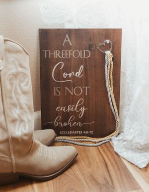 A rustic wooden sign with 'A Threefold Cord' bible verse displayed next to cowboy boots.