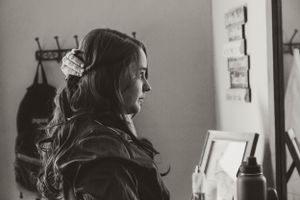 Black and white portrait of someone getting ready in a room with soft window light.