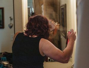 A person in black adjusts their hair while holding a drink.