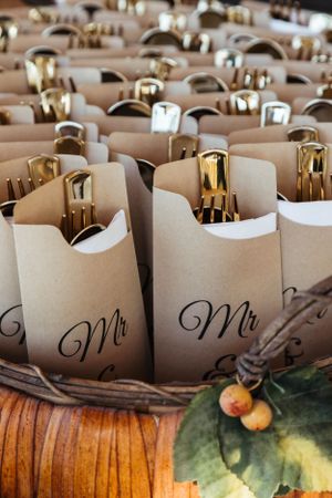 Kraft paper favor bags with 'Mr' calligraphy text and gold bottles arranged on a rustic wooden surface.