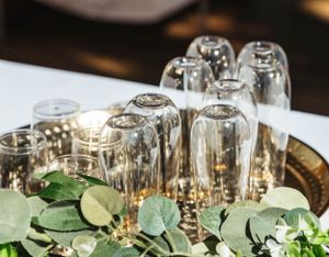 Wine glasses turned upside down on a table decorated with fresh eucalyptus leaves and candlelight.