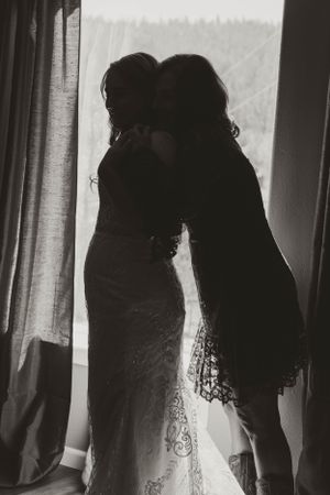 A silhouetted black and white artistic photo of two figures embracing by a window with curtains.