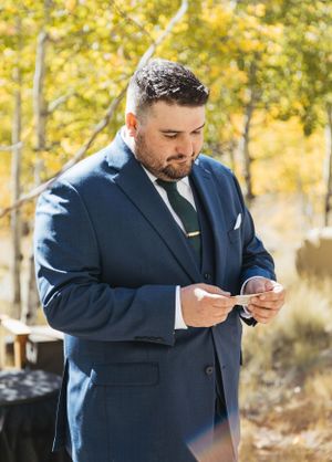 A person in a navy blue suit checks their phone during an outdoor autumn wedding.