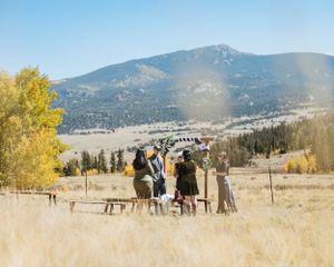 A small group stands together in a golden autumn field with mountains and fall foliage in the background.