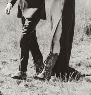 Black and white vintage photo showing two pairs of legs wearing contrasting dress shoes and cowboy boots.