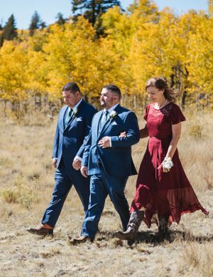 Wedding attendants walk together through autumn field with yellow aspen trees in background.