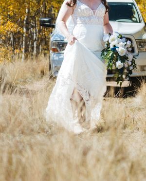 A white lace wedding dress and bouquet captured in motion through tall golden grass on a fall day.