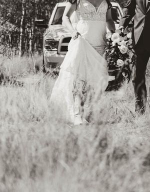 A vintage black and white photo showing the bottom half of a lace wedding dress in a field.