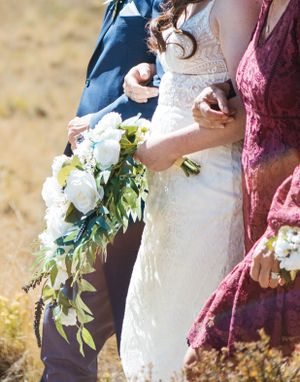 Close-up of wedding attire and a cascading white floral bouquet with greenery.