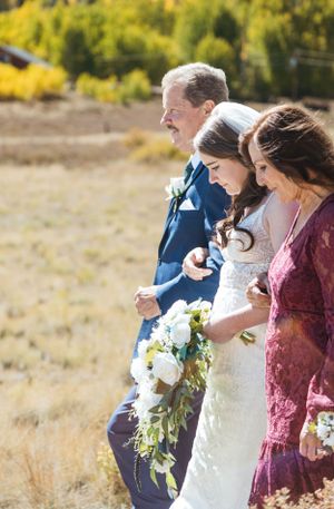 Wedding party members in formal attire stand together outdoors in autumn with a white floral bouquet.
