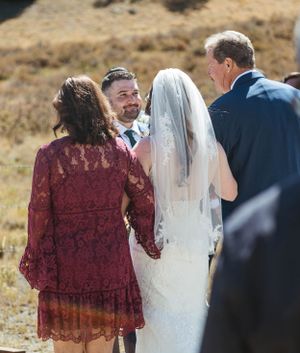 A wedding ceremony takes place outdoors in a natural setting with people gathered on a mountainside.