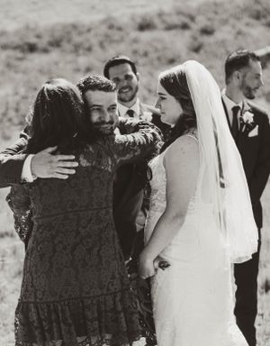 A heartfelt embrace shared between wedding guests and a bride in a flowing white veil captured in black and white.